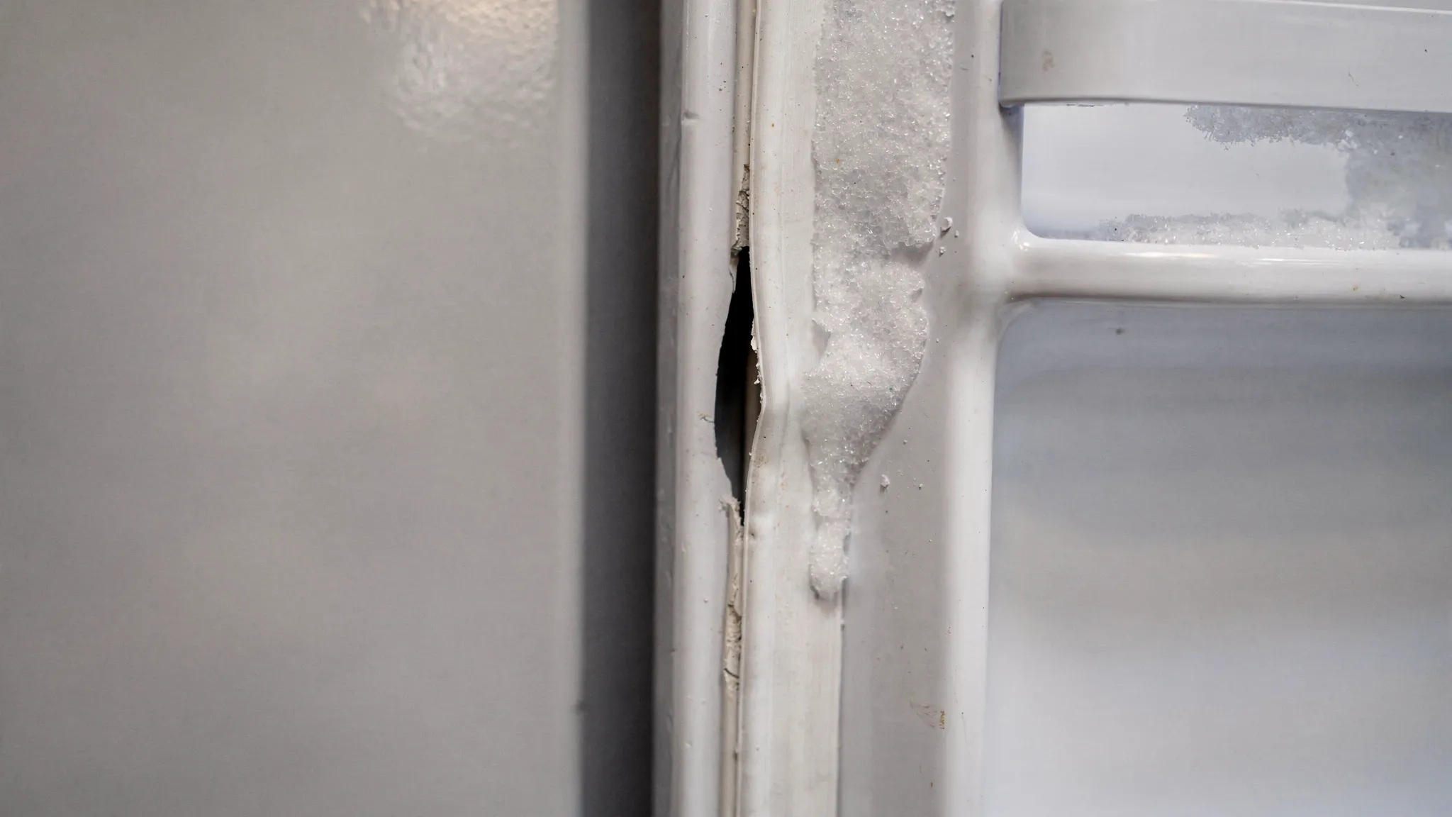 Close-up of a refrigerator door gasket with a visible tear and flattened sections, plus light frost buildup along the inside edge of the freezer compartment.