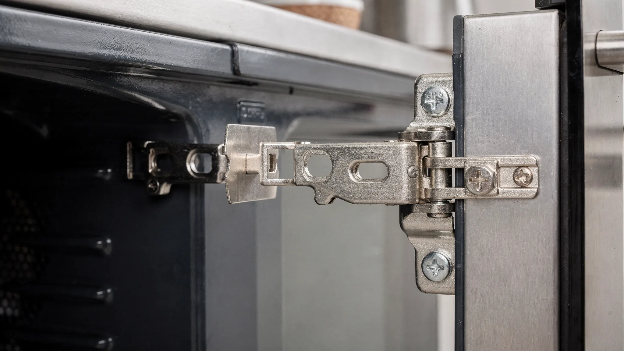 Close-up of an oven door hinge area with hinge arms and flip-style hinge locks visible, showing how the hinge lock tab positions change between unlocked and locked.