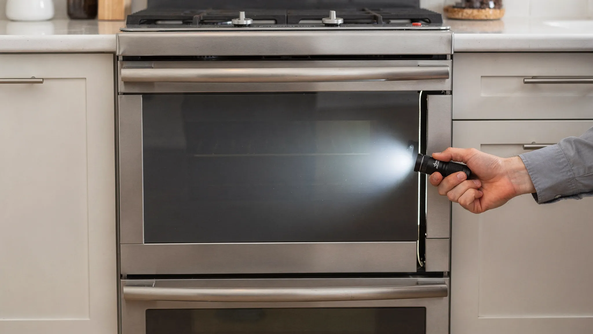 Front view of a freestanding kitchen oven with the door closed, showing an even gap around the door and a small flashlight shining along the edge to check for uneven alignment.