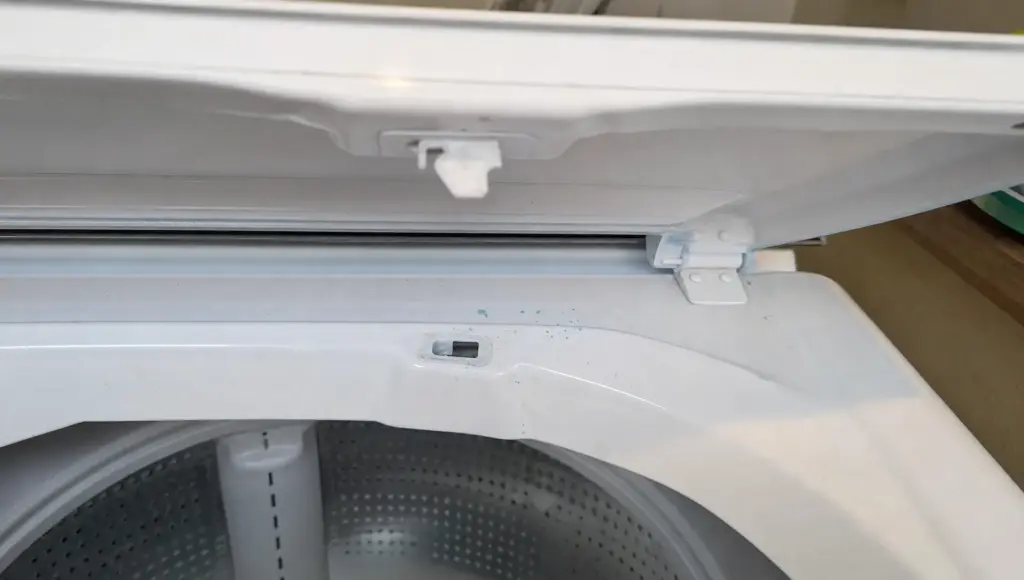 Close-up of a top-load washer lid strike and latch opening as part of a lid lock troubleshooting check.